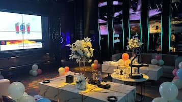 A room with a large screen, tables with floral centerpieces, and balloons.