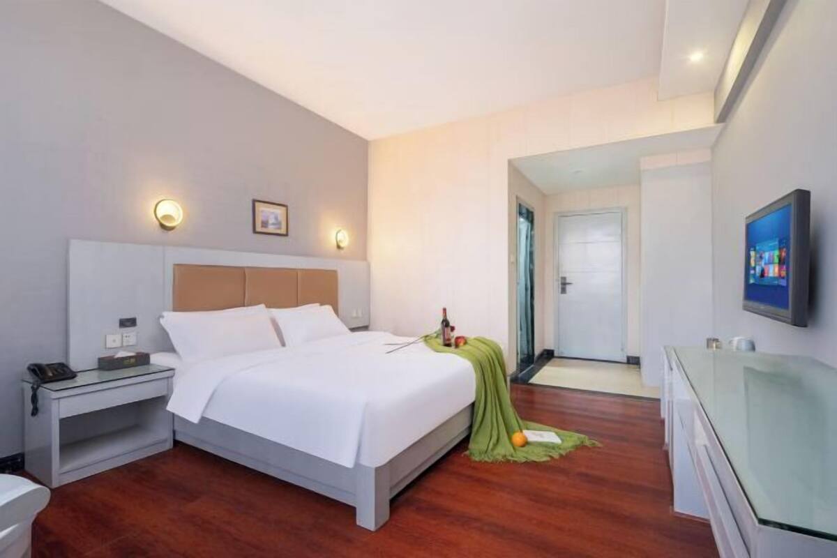 A hotel room with a bed, bedside table, lamp, and a television on the wall.