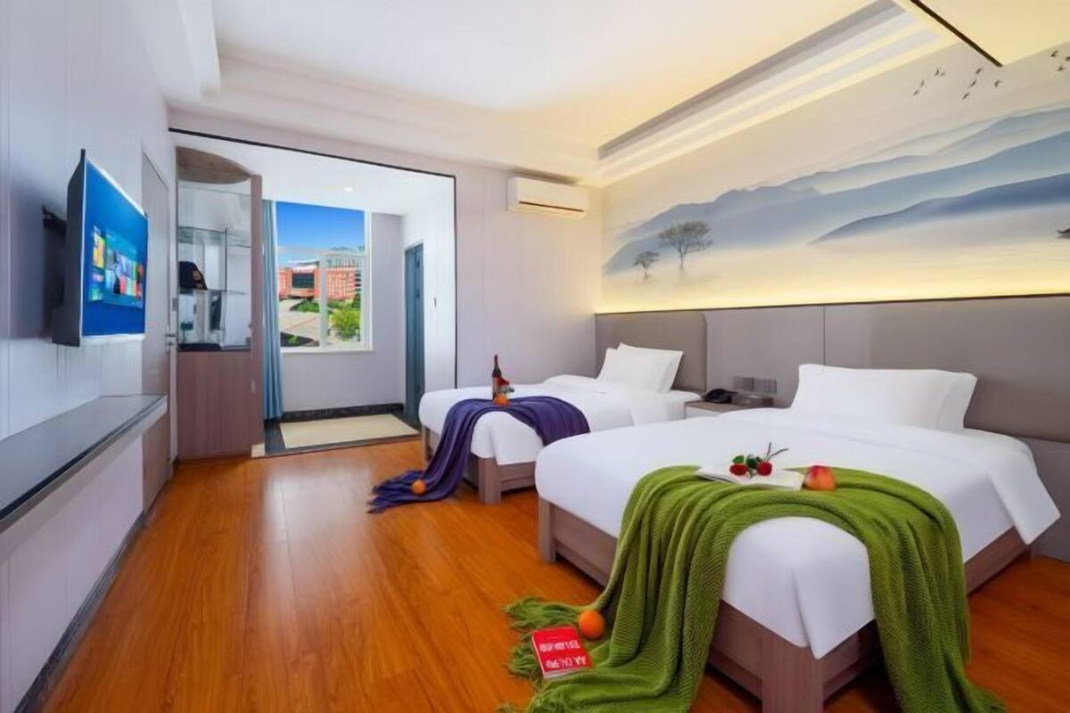 A hotel room with two beds, a flat-screen TV, and a mural of a landscape.
