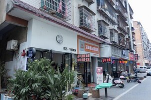 Une rangée de boutiques avec leurs enseignes, un scooter garé devant, et un immeuble à plusieurs étages.
