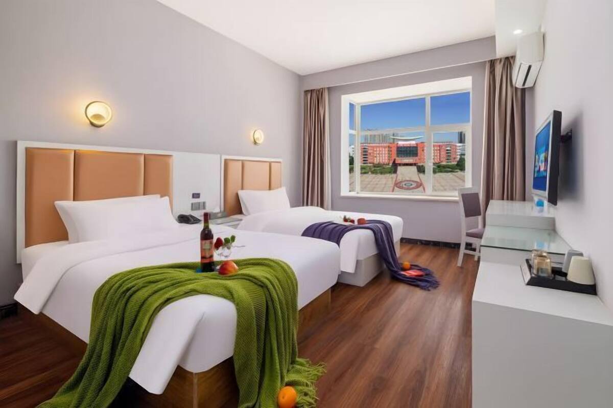 A hotel room with two beds, a desk, a chair, a TV, and a window with a view of buildings.