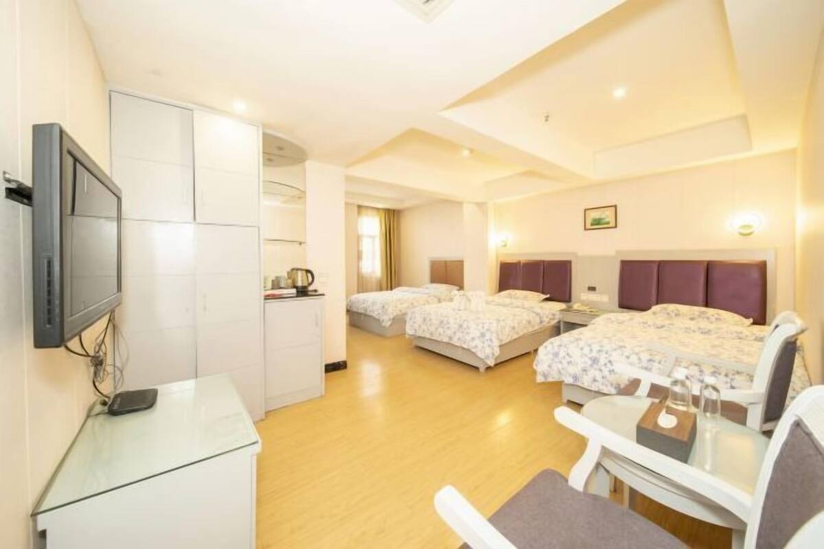 A hotel room with two beds, a desk, a TV, and a kitchenette.