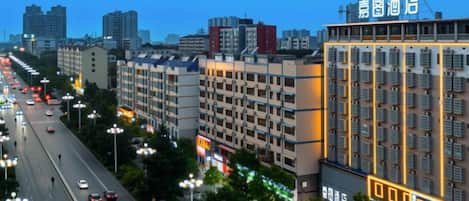 A multi-story hotel with a row of rooms on the ground floor, a parking area, and a street view with cars and streetlights.