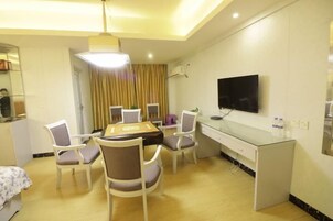 A hotel room with a dining area, a TV mounted on the wall, and a small desk with a chair.