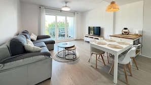 A modern living room with a sofa, coffee table, dining table, and TV.