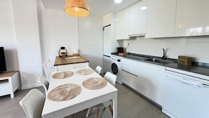 A modern kitchen with white cabinets, a washing machine, and a dining area with a table and chairs.