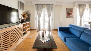 A living room with a large flat-screen TV, a blue sofa, a wooden entertainment unit, and a glass coffee table. - PUSHE Granada Plaza Menorca Art & Tradition (Granada)