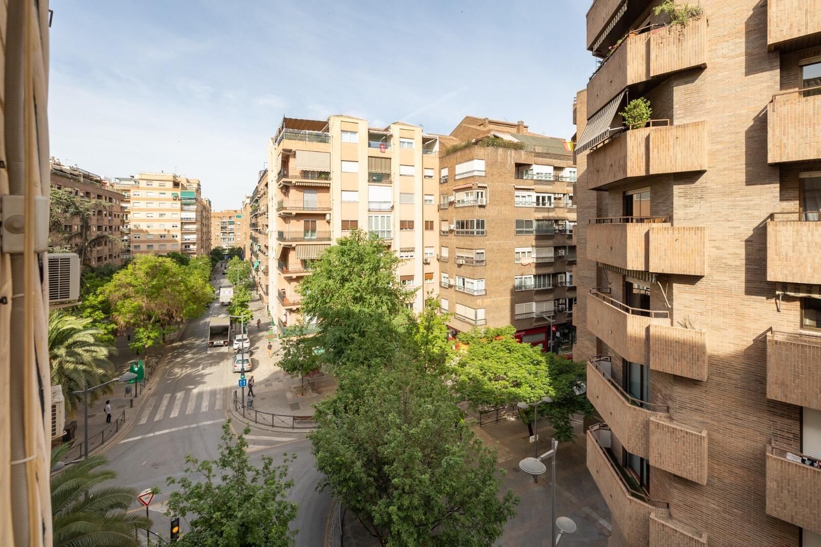 A multi-story residential building with balconies, a pedestrian street, and surrounding greenery.