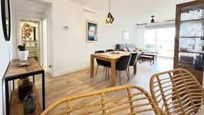 Una sala de estar moderna con comedor, que incluye una mesa de madera, sillas de mimbre y un ventanal con vistas.
