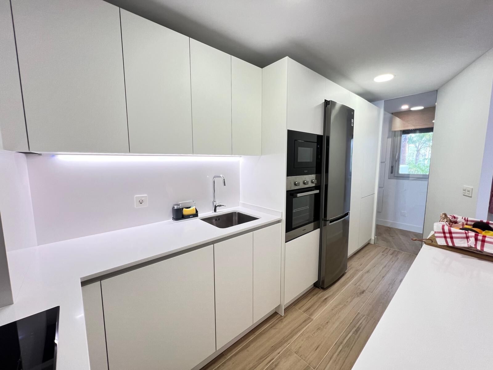 Una cocina moderna con armarios blancos, un refrigerador de acero inoxidable y un horno empotrado.