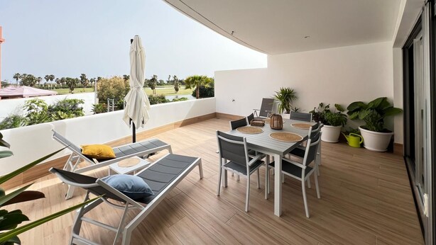 Un balcón con mesa de comedor, sillas, sillones de descanso y plantas en macetas.