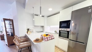 Una cocina moderna con armarios blancos, un refrigerador de acero inoxidable, horno empotrado y una isla central con taburetes de bar.