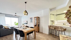 Un espacio moderno con comedor, cocina y zona de estar con sofá y sillones.