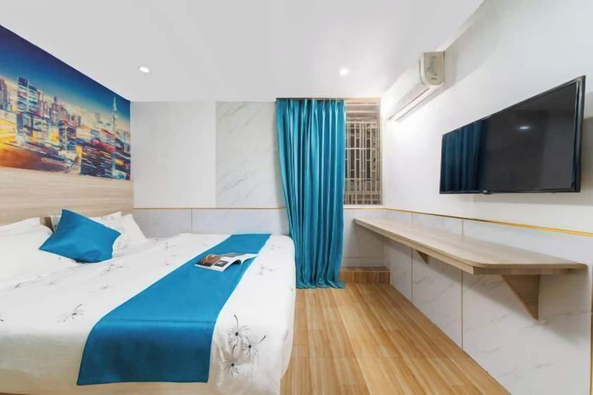 A hotel room with a bed, a TV, a desk, and a cityscape painting on the wall.