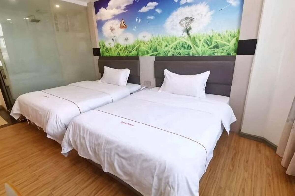 A hotel room with two beds, a mural of a field with dandelions, and a wooden floor.