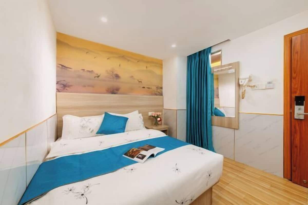 A hotel room with a bed, a nightstand, a mirror, and a door.