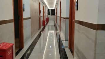 A hotel corridor with doors on both sides, a red trash bin, and a polished floor.