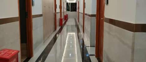 A hotel corridor with doors on both sides, a red trash bin, and a polished floor.