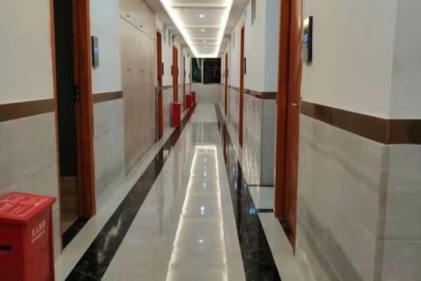 A hotel corridor with doors on both sides, a red trash bin, and a polished floor.