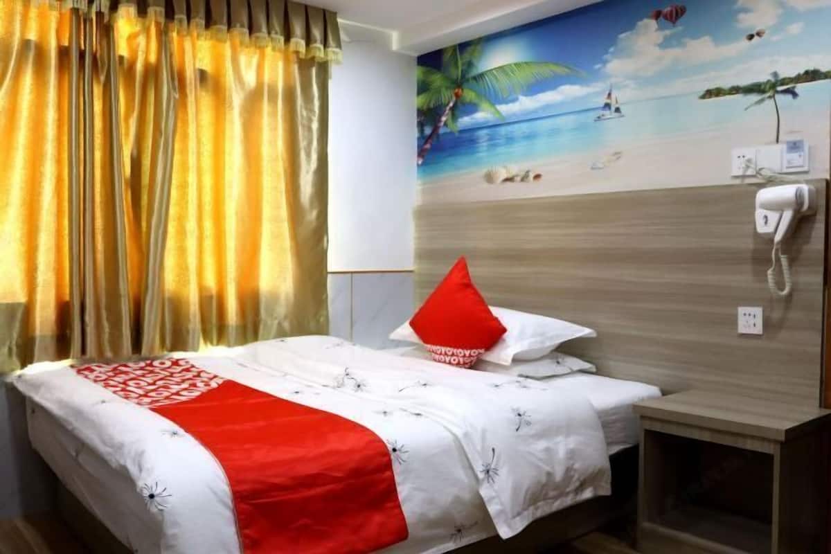A hotel room with a bed, a wall-mounted phone, and a beach-themed mural.