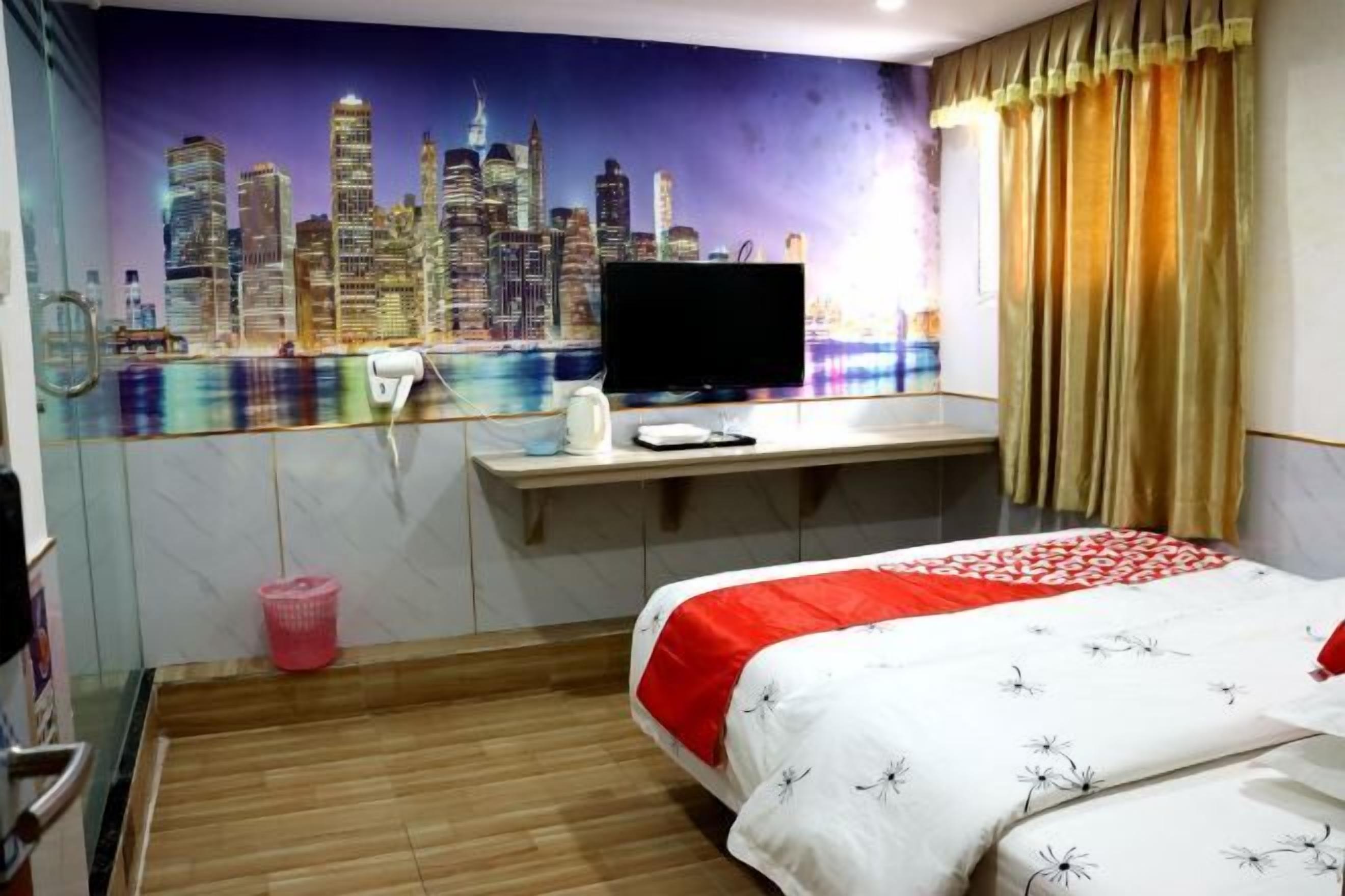 Une chambre d’hôtel avec une fresque représentant un paysage urbain, un lit recouvert d’une courtepointe rouge et blanche, un bureau avec une télévision et une fenêtre avec des rideaux.
