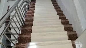 Un escalier dont les marches alternent entre le blanc et le marron, avec des rampes en métal et un couloir droit et étroit.