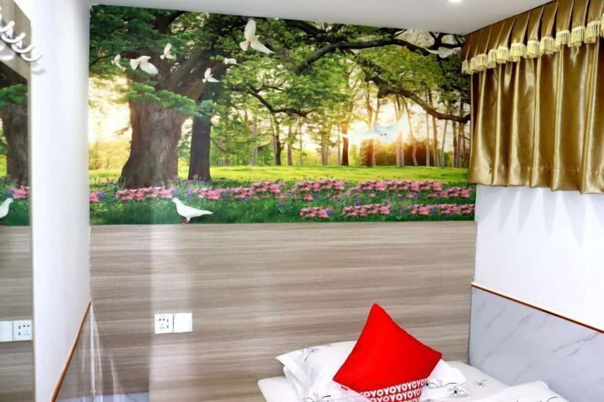 A bedroom with a mural of a forest scene, a bed with white bedding and a red pillow, and a gold curtain.