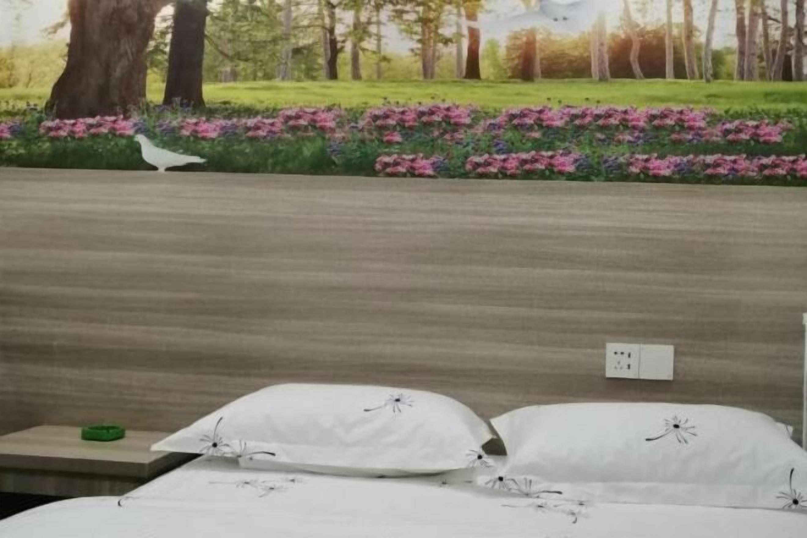 A bedroom with a bed, pillows, a nightstand, and a wall mural.