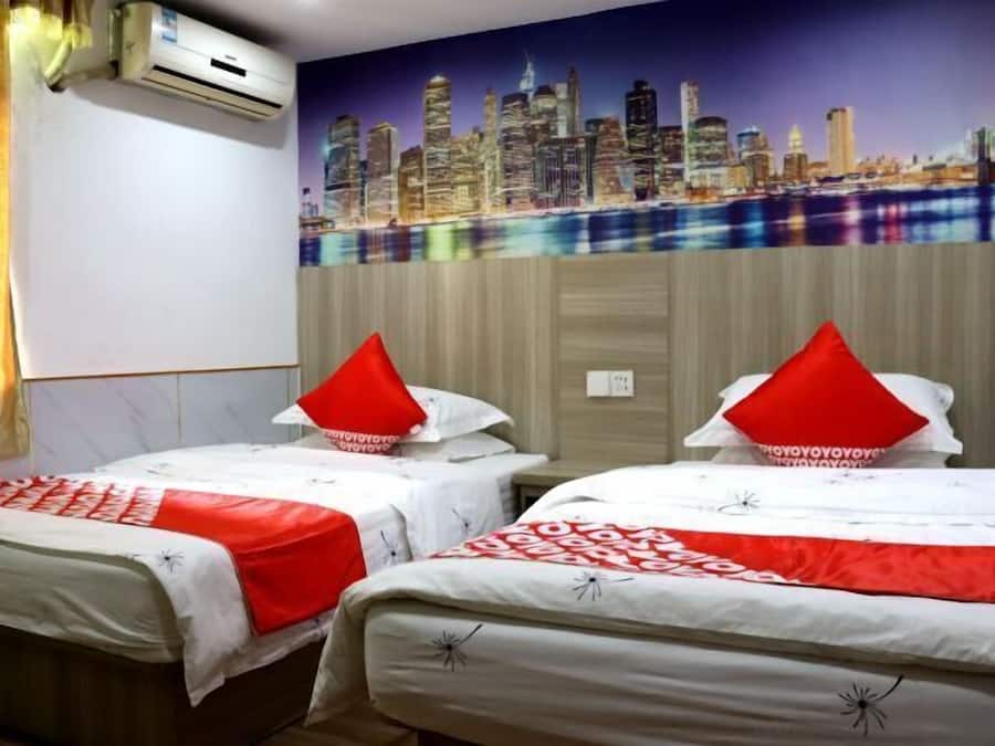 A hotel room with two beds, each with a red pillow, a cityscape mural on the wall, and an air conditioning unit.
