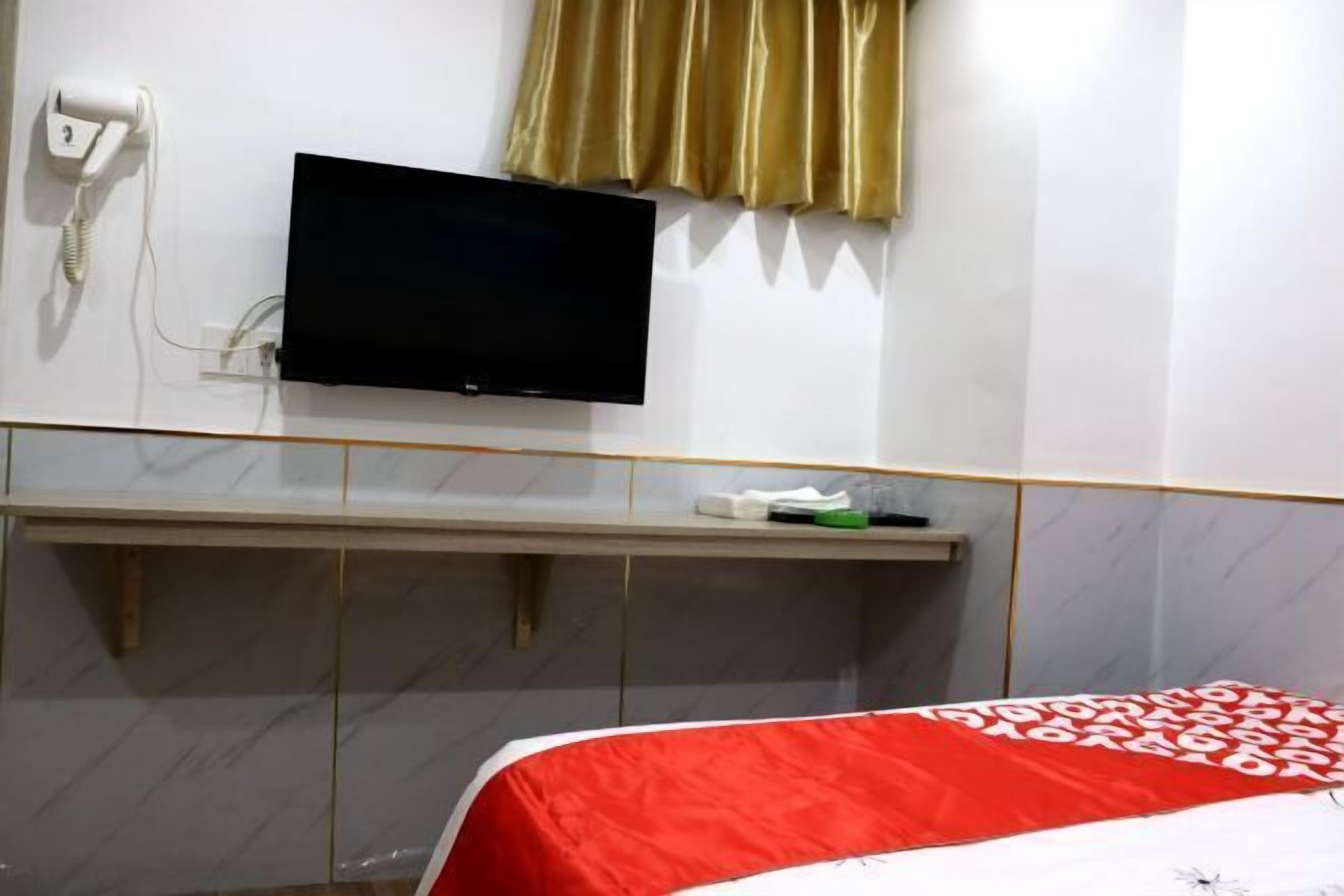 Une chambre d’hôtel avec un lit, un téléviseur fixé au mur, un téléphone et une fenêtre avec des rideaux.