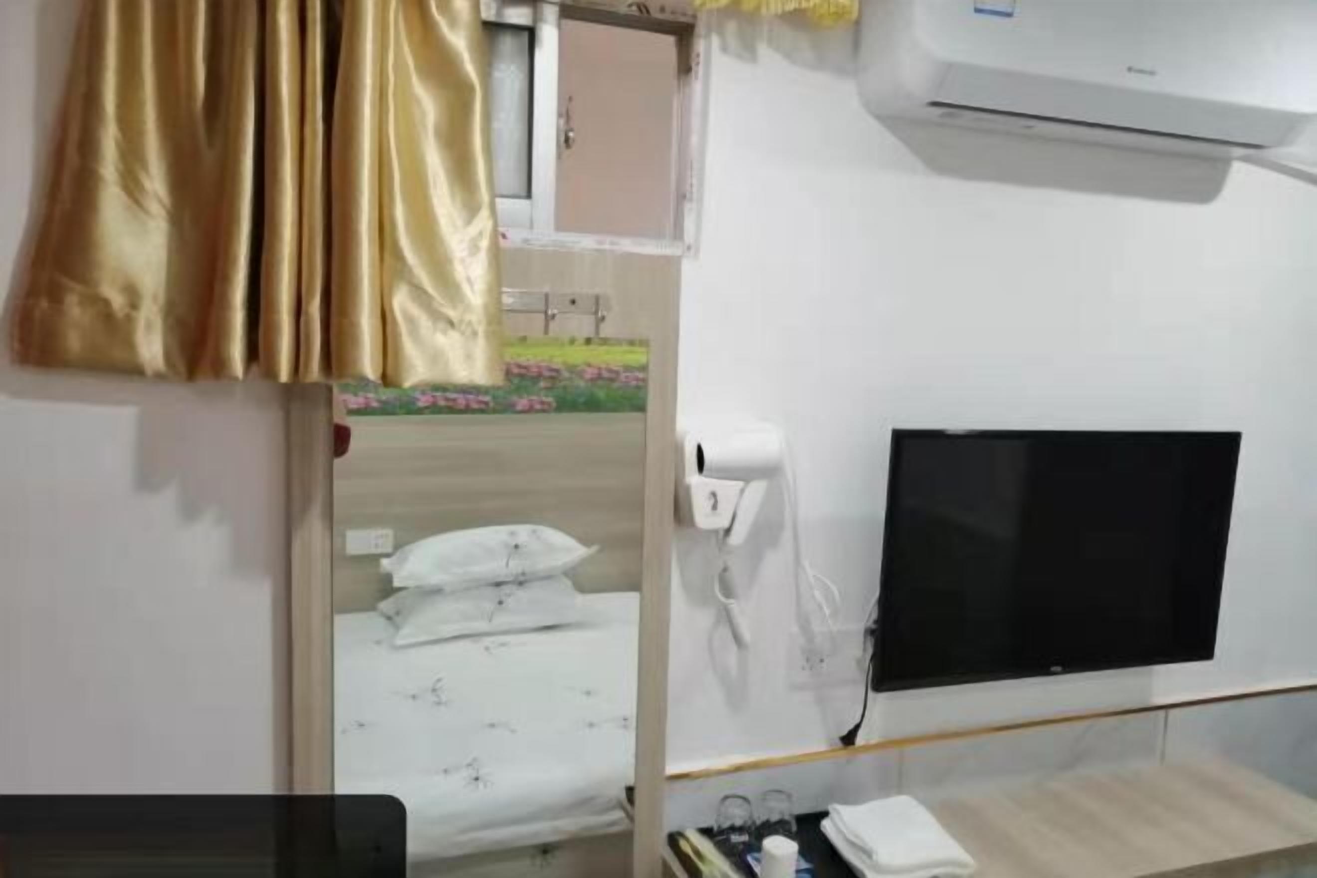A hotel room with a bed, a TV mounted on the wall, an air conditioning unit, and a window with curtains.