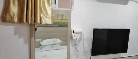 A hotel room with a bed, a TV mounted on the wall, an air conditioning unit, and a window with curtains.