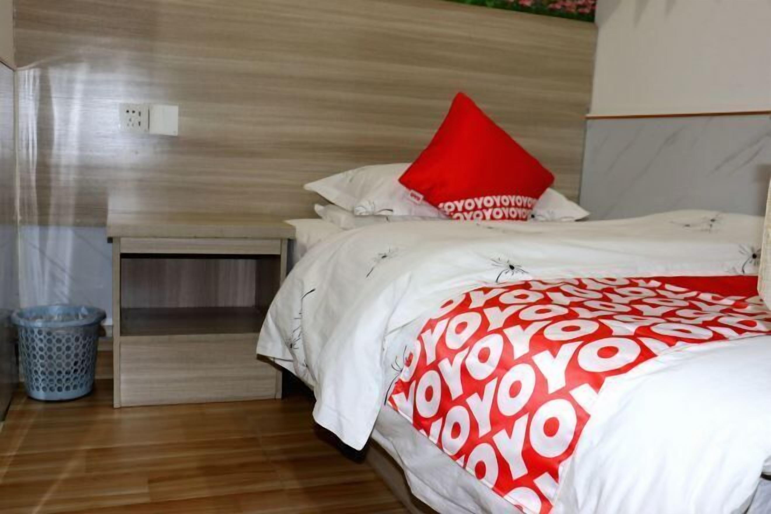 A hotel room with a bed, a nightstand, a trash bin, and a wooden floor.