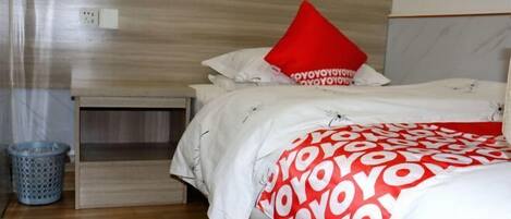 A hotel room with a bed, a nightstand, a trash bin, and a wooden floor.