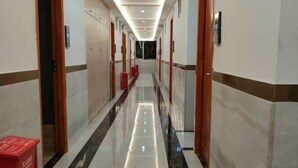 Un couloir d’hôtel avec un sol en marbre brillant, des portes en bois et des poubelles rouges.