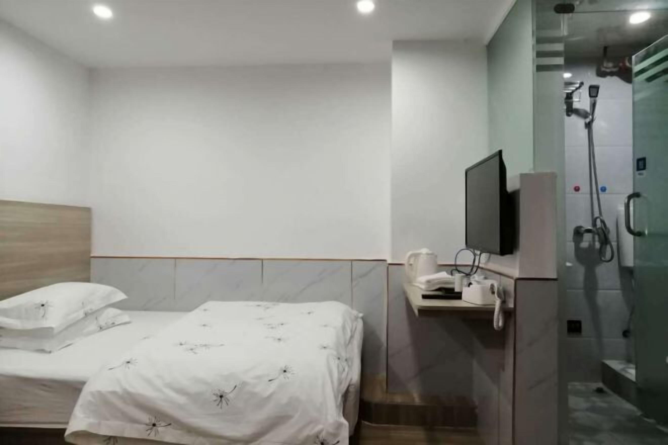 A hotel room with a bed, a TV, a coffee machine, and a shower area.