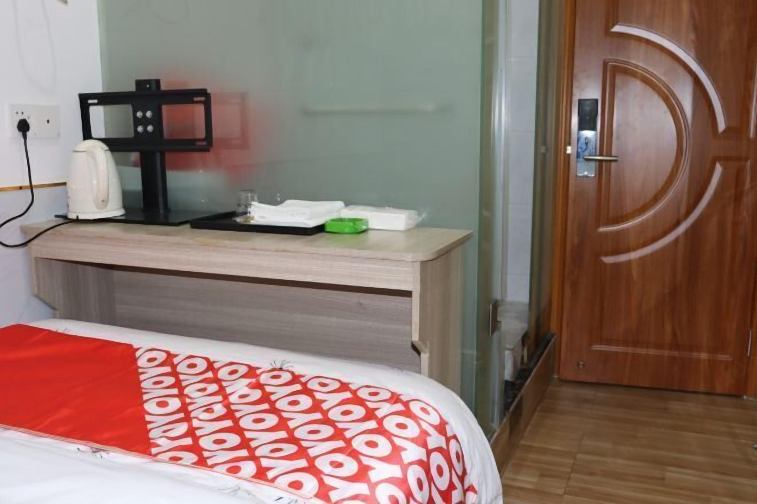 A hotel room with a bed, a desk with a coffee maker, a door with a decorative handle, and a small green object on the desk.