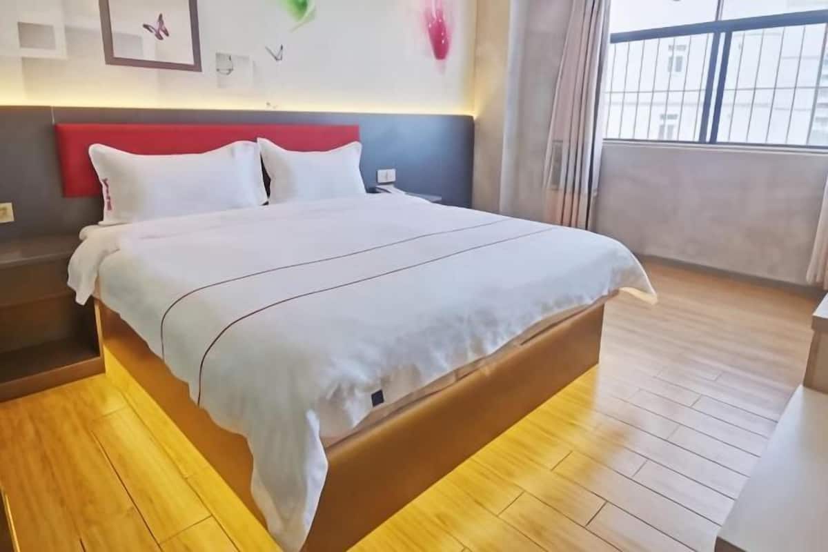 A neatly made bed with a white bedspread and pillows, a wooden headboard, and a view of the outdoors through a window.