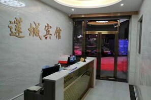 A reception desk with a glass partition, a wall with Chinese characters, and a view of parked cars outside. - LianChen Hotel（Shenzhen North Railway Station） (Shenzhen)