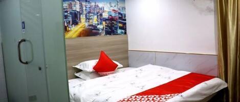 A hotel room with a bed, a cityscape mural, a red pillow, and a glass door.
