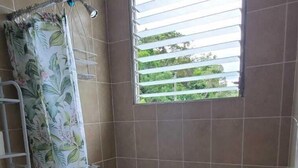 A bathroom with a toilet, a shower with a curtain, a window with blinds, and tiled walls. - Villa Lorena Casa de Huespedes (San Salvador)
