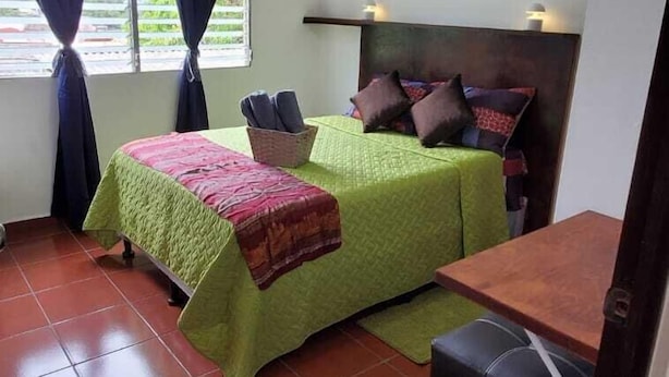A small, well-lit room with two beds, a ceiling fan, and a window with curtains. - Villa Lorena Casa de Huespedes (San Salvador)