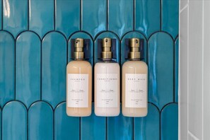 Three bottles of shampoo, conditioner, and body wash against a blue tiled wall. - Location! w/King Beds+Hot Tub+GameRoom+Theater+Gym+Fire Pit (Prairie Village)