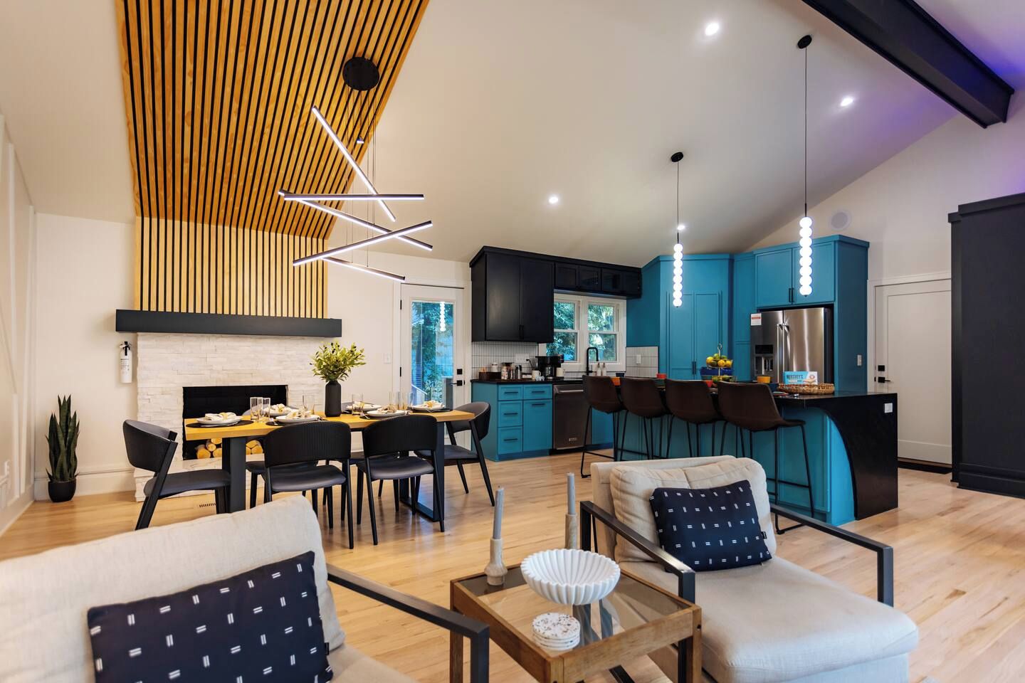 A modern kitchen with blue cabinets, a dining area with a wooden table and chairs, and a living room with a sofa and a coffee table.
