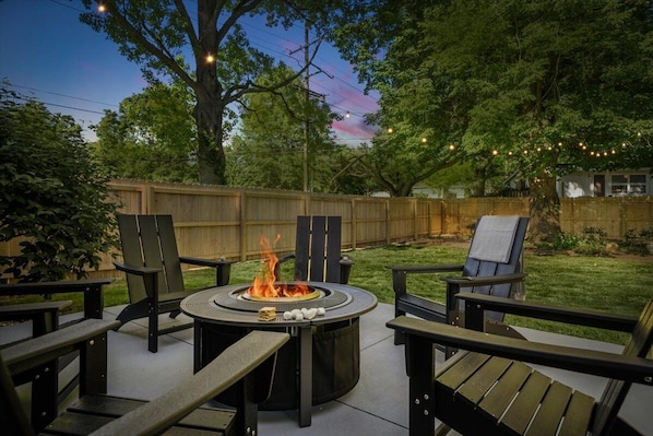 A backyard with a circular fire pit table surrounded by four Adirondack chairs. - Location! w/King Beds+Hot Tub+GameRoom+Theater+Gym+Fire Pit (Prairie Village)