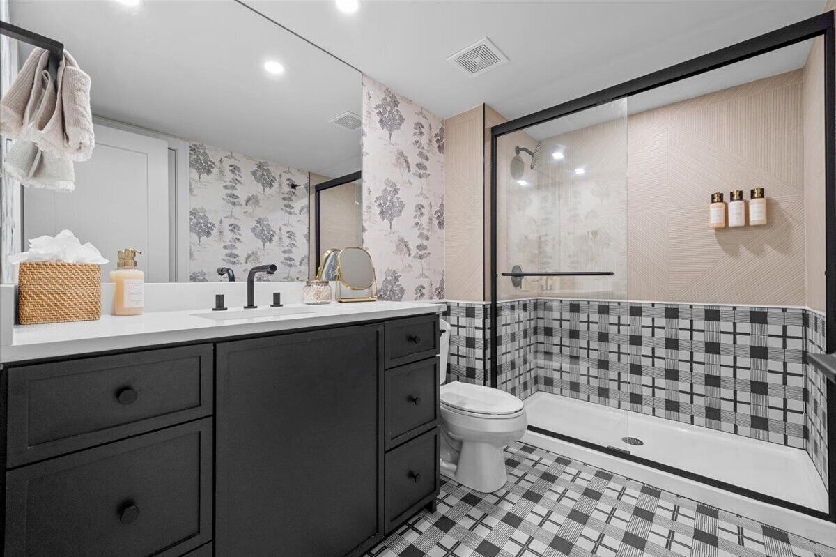 A modern bathroom with a black and white checkered floor, a large mirror, a white toilet, and a shower area with a glass door.