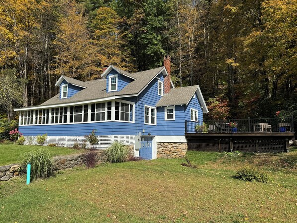 A blue house with a stone foundation, a porch, and a deck.