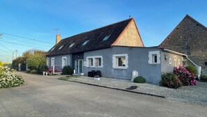 Et tosset hus med en grå facade, et tegltag og en grusvej.