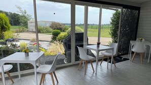 En moderne terrasse med hvide møbler, en glasdør til en have, og udsigt over landskabet.