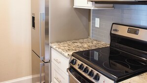 A kitchen with a stainless steel refrigerator, a microwave, a stove, and white cabinets.